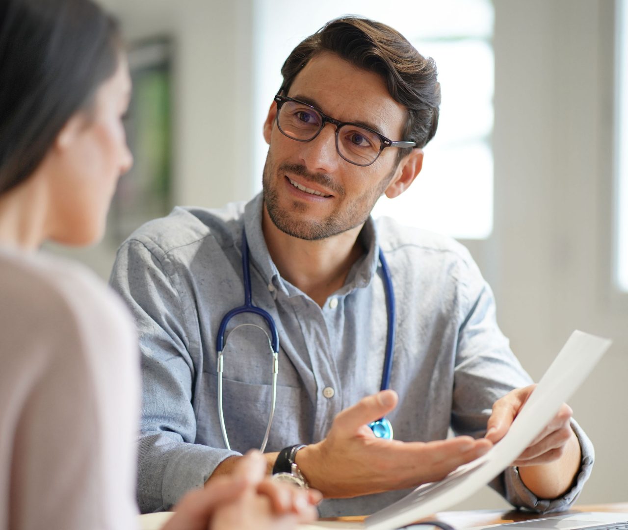 Photo of modern young doctor speaking to patient in office
