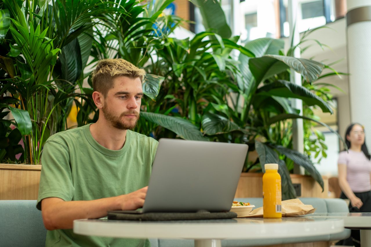 A student sitting at their laptop while eating lunch on Kensington Campus